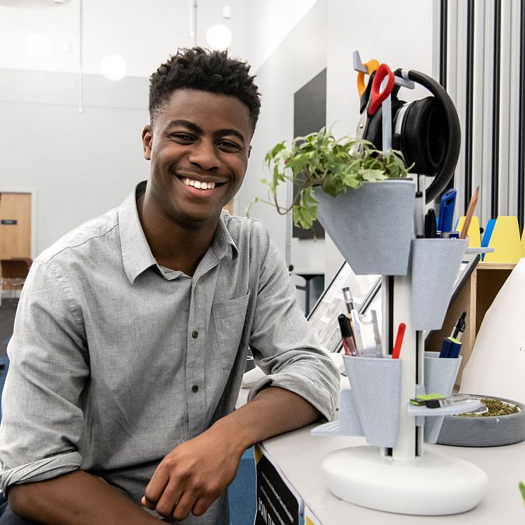 Emmanuel Oyemade smiles while seated next to his innovative new desk tidy system, Modomise.