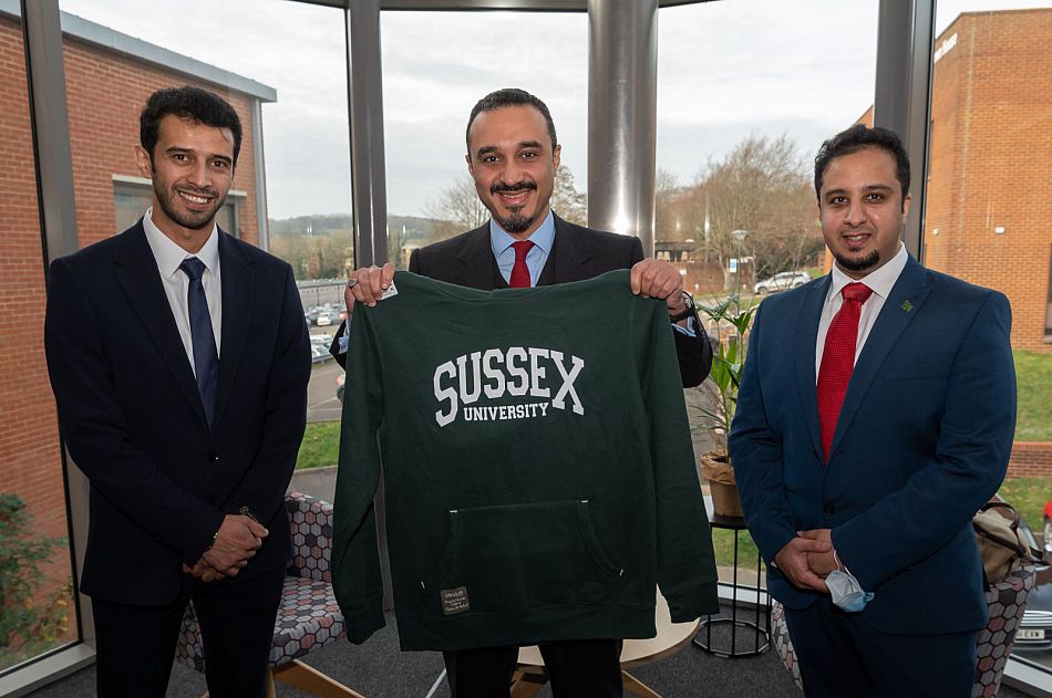 3 men hold up a Sussex University Sweatshirt