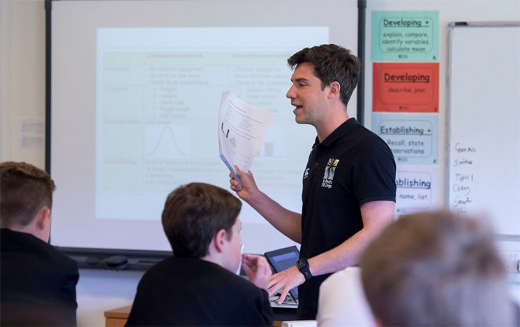 Secondary school teacher standing at front of class, presentation on screen in the background