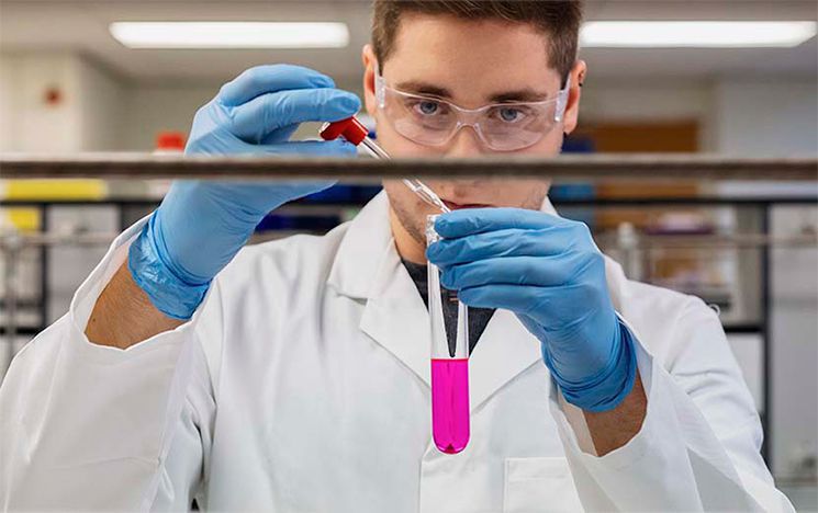 Student in lab coat using pipette and test tube