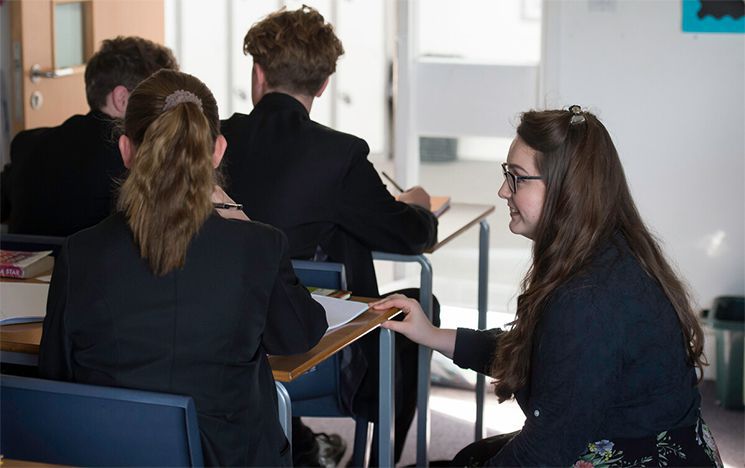 Teacher knelt by a student at her desk and helping her