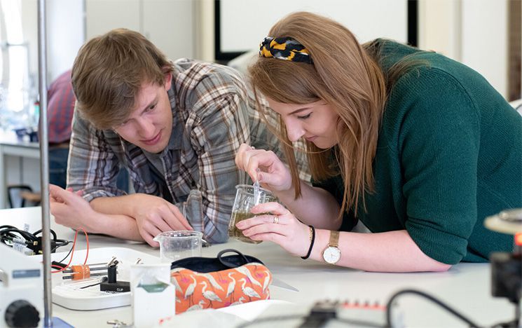 Two students in a science lab using a pipette and beaker