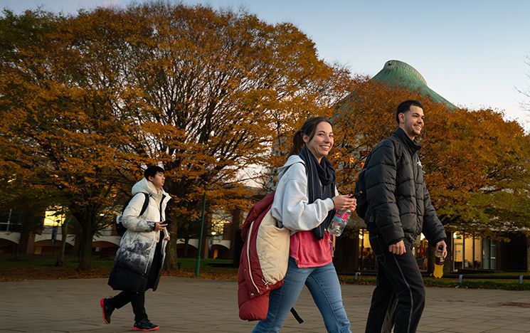 Smiling students walk past the Meeting House with autumnal trees in the background