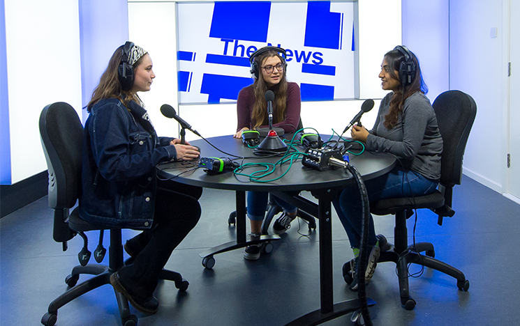 A group of journalists sitting round a table in a studio in front of microphones.