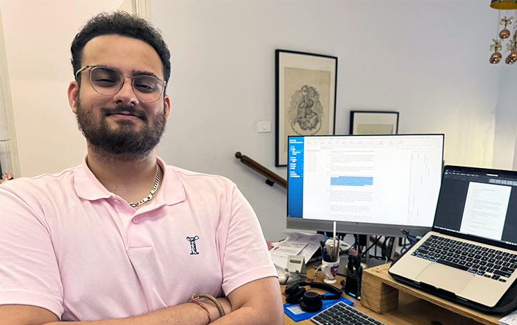 Adwait-Vaishnavi sitting in front of two computer screens, facing the camera with his arms folded.