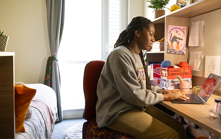 A student sitting in their uni accommodation at a desk in front of a laptop