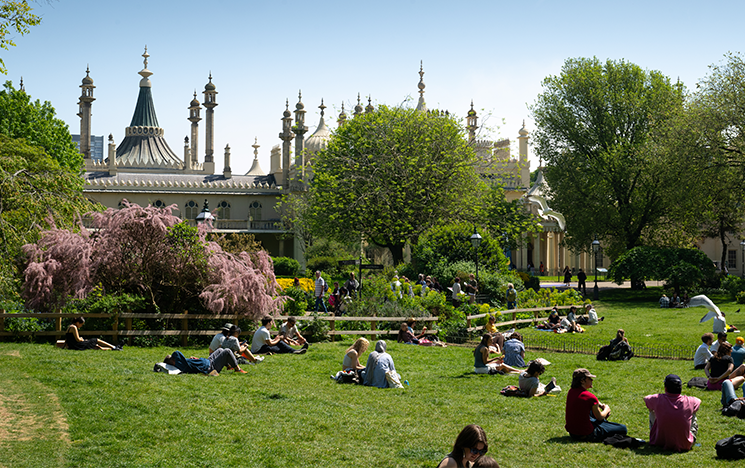 People sitting on the grass outside Brighton Pavilion in the sunshine