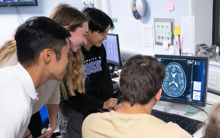 Summer School students huddle round an image of a brain on a monitor