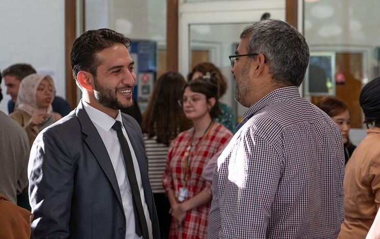 Two people talking at a reception event with others in the background