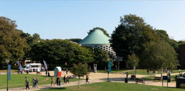 A sunny day on campus, overlooking library square. The meeting house is in the background and students are walking in the foreground.