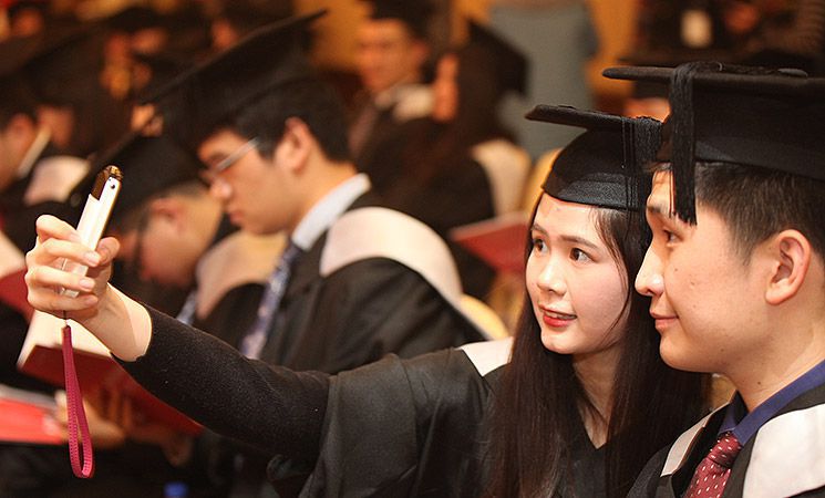 Two graduates pose for a selfie at an overseas celebration