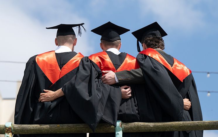 Three graduates in robes facing away from the camera, with their arms around each other.