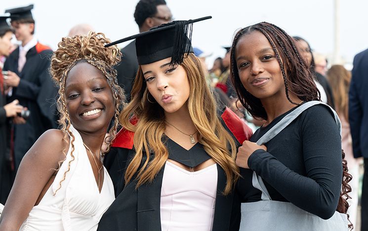 A graduate in gown standing outdoors with two companions.