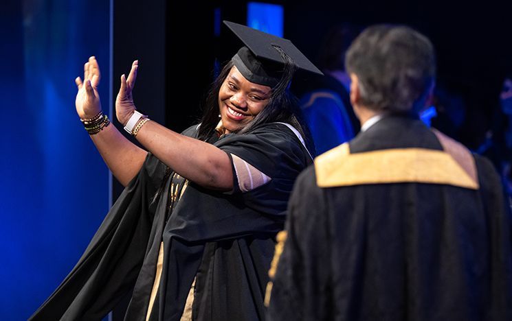 A graduate lifts both arms on a blue‑lit stage.