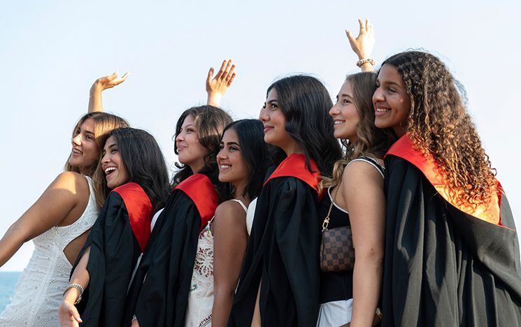 Seven people, some in gowns and some in white dresses, pose and celebrate outdoors.