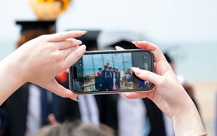 A phone records a group of graduates posing near the sea-front.