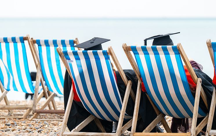 Two graduates sitting in striped deck chairs facing the sea.
