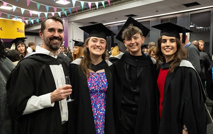 Four graduates posing indoors with bunting overhead.