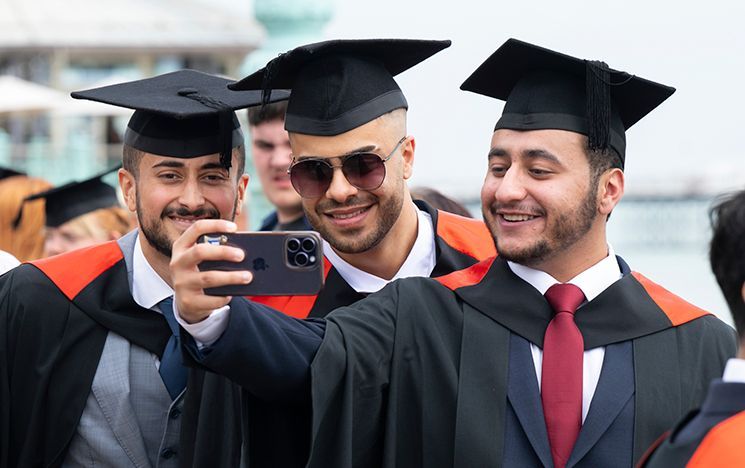 Three graduates in robes pose for a selfie