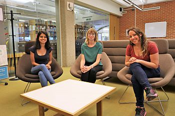 Three PhD students sit in chairs in front of a white table in Sussex Research Hive