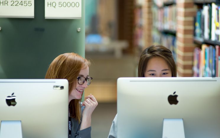 Two students sat at adjacent computers in Library