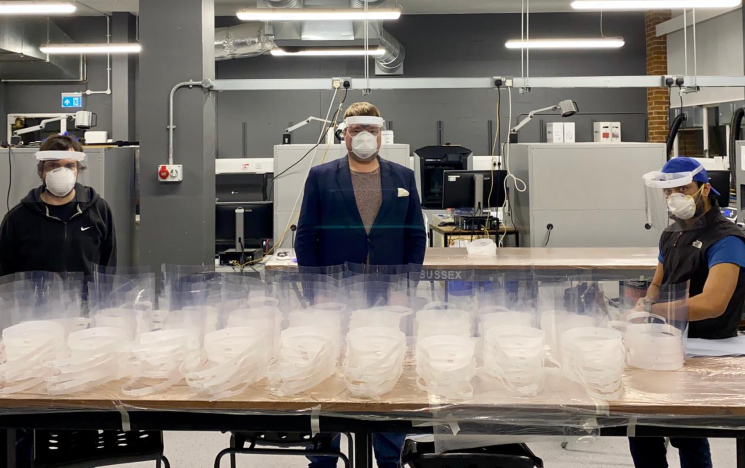 Three engineers pose with a table with hundreds of face masks