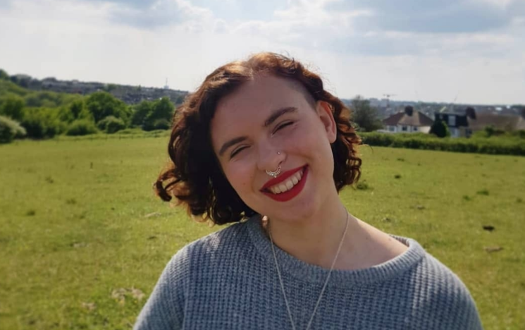 Portrait photo of Katherine White, a student involved in the Role Models scheme, smiling on a sunny day with countryside in the background