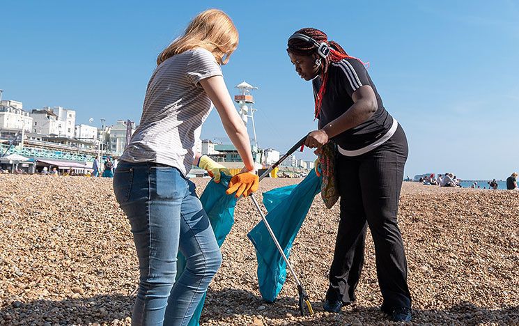 Two young people using litter pickers and bin bags to clean Brighton beach