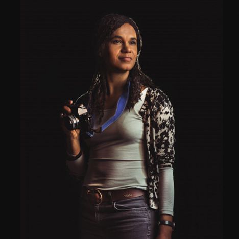 Portrait shot of Dr Pamela Kea, from the School of Global Studies, taken by alumni Miss Aniela, holding a camera as a symbol of her work as an anthropologist.