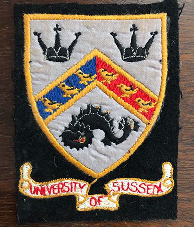 A black fabric badge, designed as a patch to sew onto cloth, bearing the University of Sussex crest.