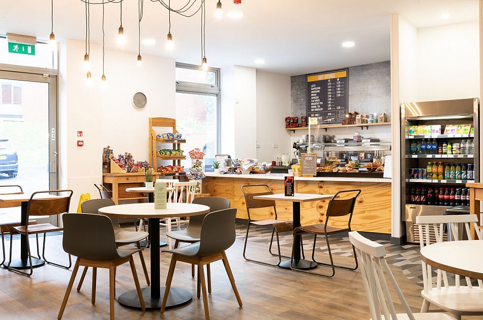 The interior of the Sussex Innovation Centre cafe showing the seating area, the fridge with drinks in it and the counter.