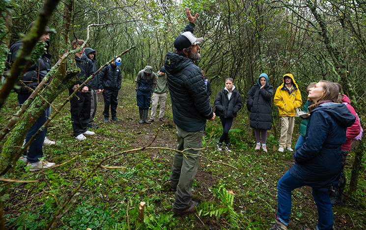 A lecturer addresses a group of students in a forest.