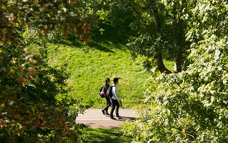 Two students walking through campus, framed by green trees.