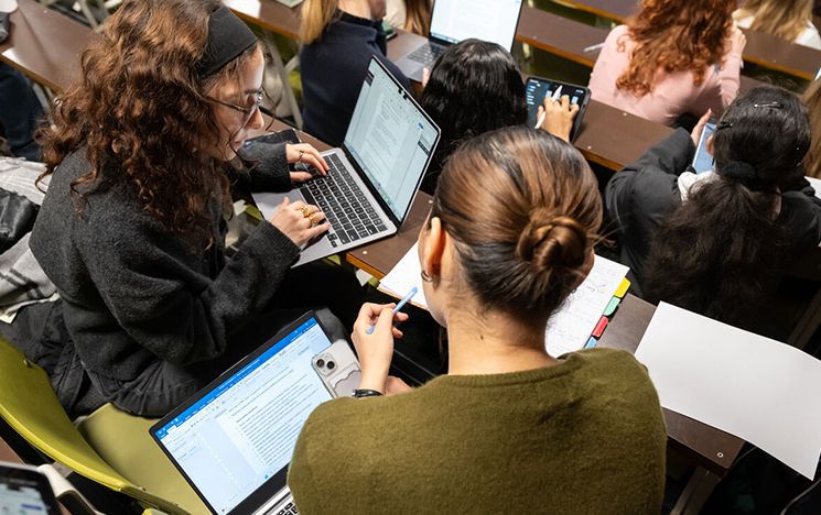 Students in a lecture hall using their laptops and discussing notes