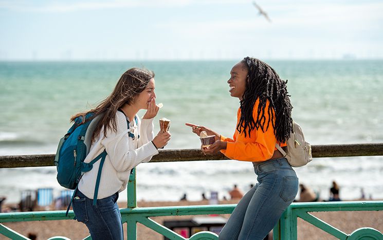 Two women laughing and eating ice cream on Brighton seafront