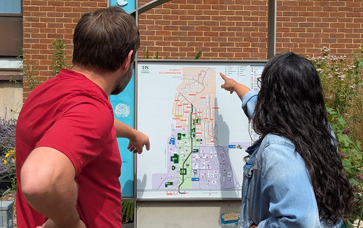 A man and woman are pictured from the back pointing at a map of campus