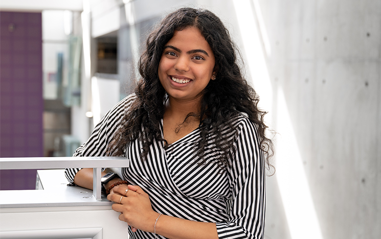 Sahana Suraj smiling at the camera, leaning against a white staircase.