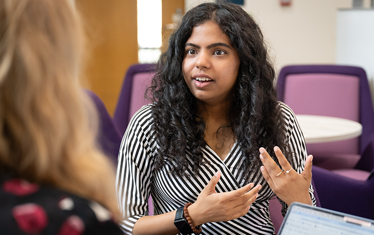 Sahana in conversation with Chloe Murphy. Sahana is demonstrating with her hands.