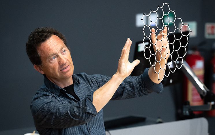 A man gestures with both hands while examining a hexagonal lattice model.