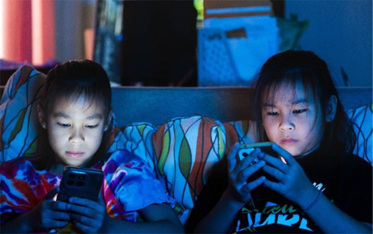 Two children sitting on a sofa on their phones