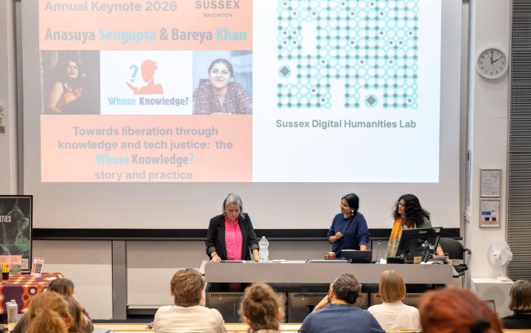 Three speakers at a lecture podium below a large presentation screen for the Sussex Annual Keynote 2026 event.
