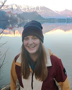 Young female pictured in front of a lake with mountains in the background