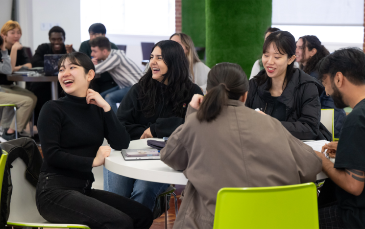 Students sitting together at a round table laughing and smiling in a seminar