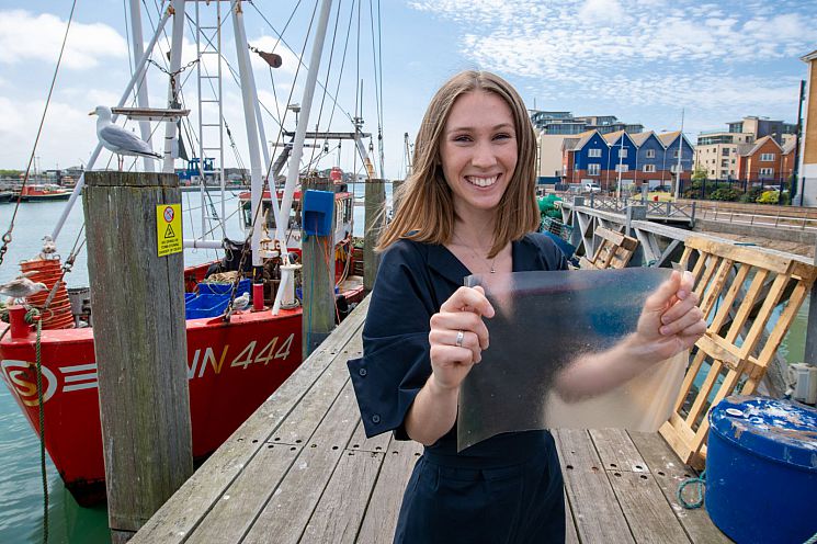 Product designer Lucy Hughes at Newhaven Harbour, holding her sustainable packaging material MarinaTex