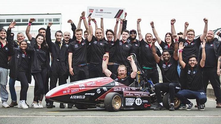 students standing around racing car, cheering