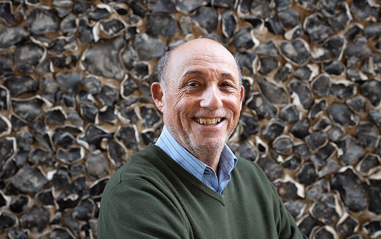 Professor Ivor Gaber, smiling at the camera, head and shoulders portrait shot, in front of campus flint wall