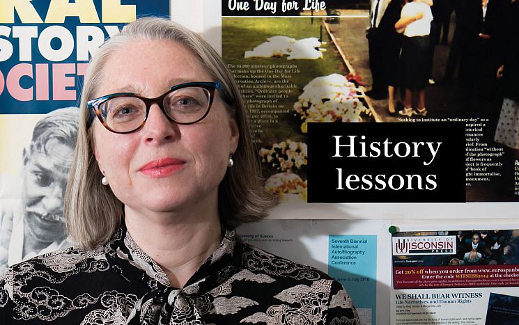 Professor Margaretta Jolly stands in front of a noticeboard with posters on and the title words of the feature History lessons