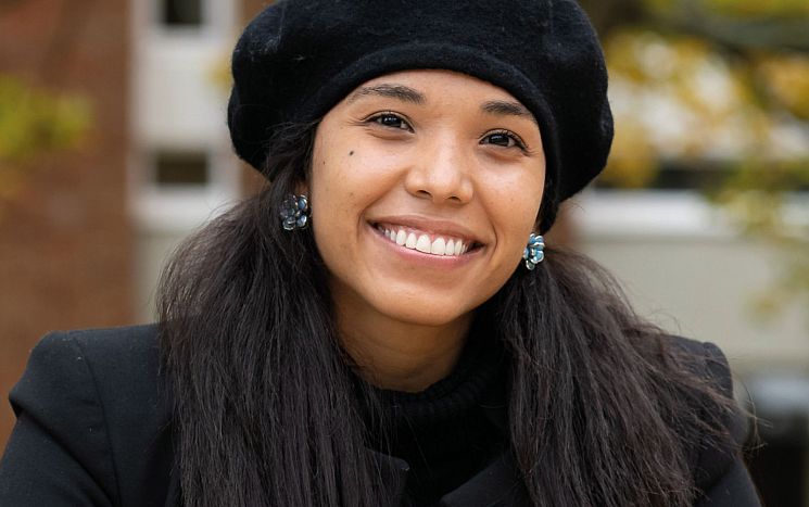 photo of current student Paula Andrea Pena, seated, smiling at camera with campus landscape in the background