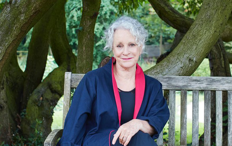 Alumni Philippa Gregory smiles, sitting on a bench in a garden.
