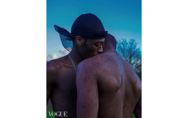 Alumna Jordi poses with his face resting on another model's shoulder in front of a blue sky